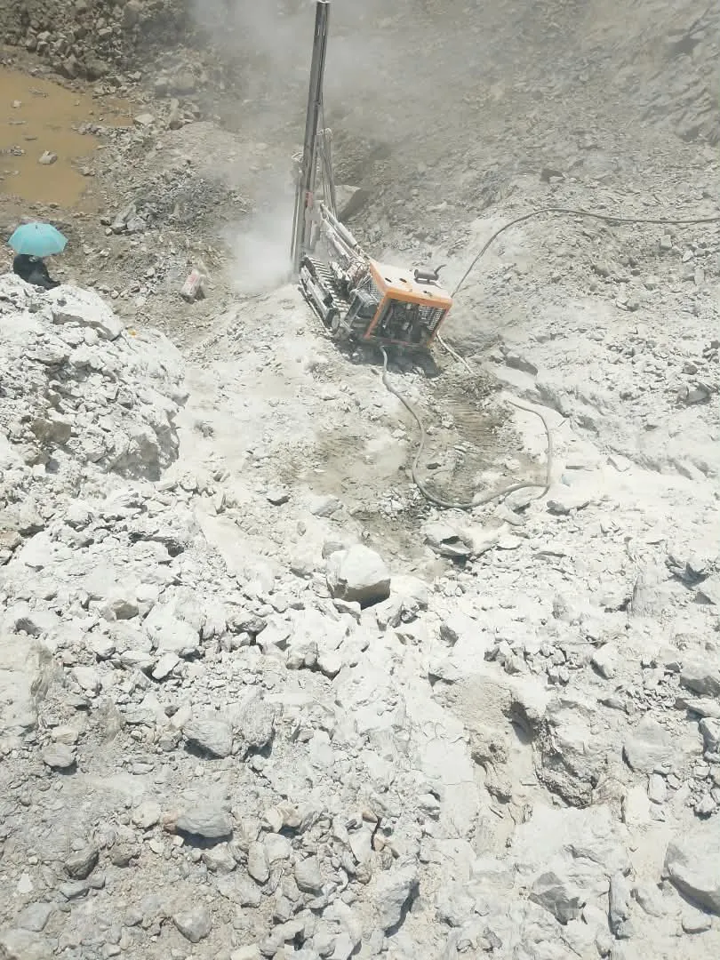Crawler drill rig drilling into rock on the pit floor, with dust rising